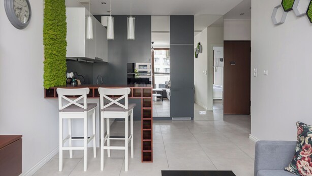 Eine moderne Küche mit weißen Barhocker, einer vertikalen grünen Wand und Blick in den Wohnbereich.