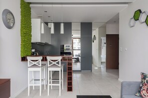 Una cocina moderna con taburetes blancos, un jardín vertical verde y vistas al salón.
