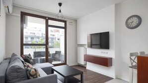 Ein modernes Wohnzimmer mit einer Couch, einem Couchtisch, einem an der Wand montierten Fernseher und einer Glastür, die zu einem Außenbereich führt.