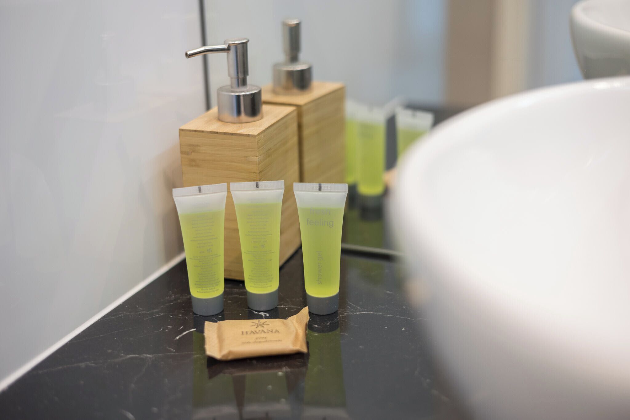 Ett badrum med en svart bänkskiva, tre tuber lotion och en dispenser för tvål gjord av trä.