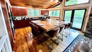 A spacious kitchen with wooden cabinets, a large island, and a dining area with a long table and chairs. - Cabin with Mountain Views / Large Deck / Fireplace / Near Hiking, Biking, Winery (Beech Mountain)