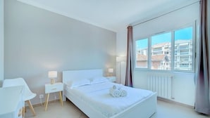 Un dormitorio moderno con una cama grande, mesitas de noche, un escritorio y una ventana con cortinas.