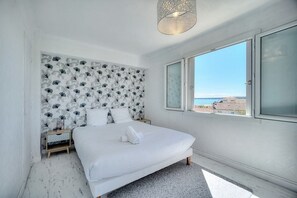 A bedroom with a large bed, a nightstand, a decorative wall, and a window with a view.