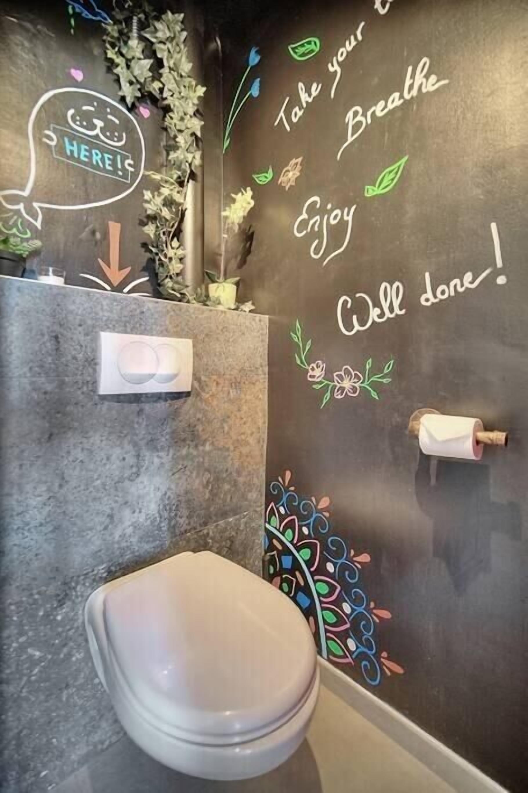 Une salle de bain moderne équipée de toilettes, d’un sèche-mains et d’un mur orné de phrases motivantes et d’éléments décoratifs.