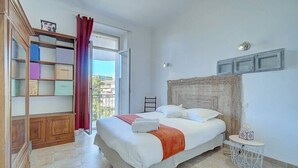 A bedroom with a bed, a wooden wardrobe, a small round table, and a view of the outside. - Upstays Quiet Center 60m² Apartment (Cannes)
