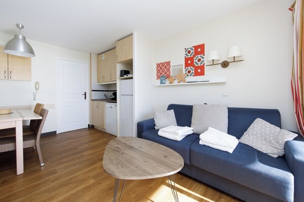 Un espace de vie compact comprenant un coin cuisine, un coin repas et un espace détente avec un canapé et une petite table ronde.