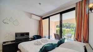 A hotel room with a large bed, a TV, and a balcony with curtains.