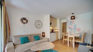 A modern living room with a sofa, coffee table, and dining area with chairs. There is a kitchen in the background.