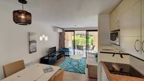 A modern kitchen with a microwave, stove, and cabinets. There is a dining area with a table and chairs, and a living area with a sofa and TV.