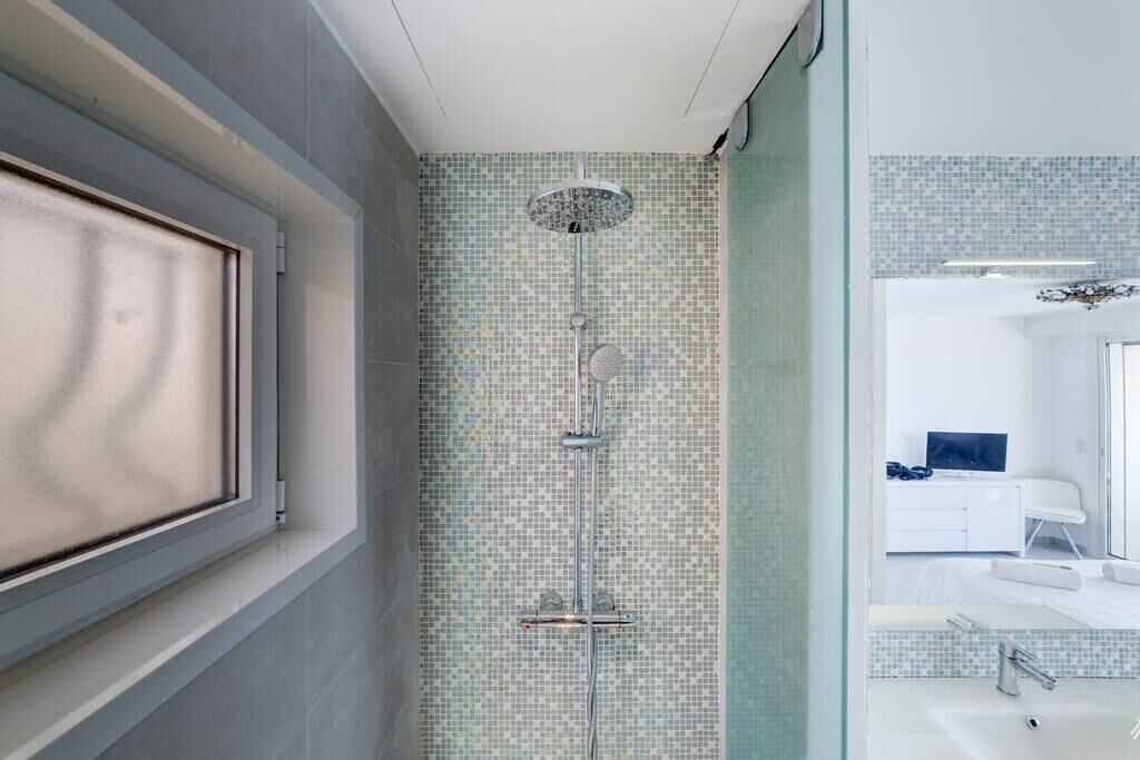 A bathroom with a shower, tiled walls, a window, and a sink.