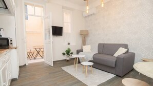 Een moderne woonkamer met een grijze bank, een klein rond tafeltje en een aan de muur bevestigde televisie.