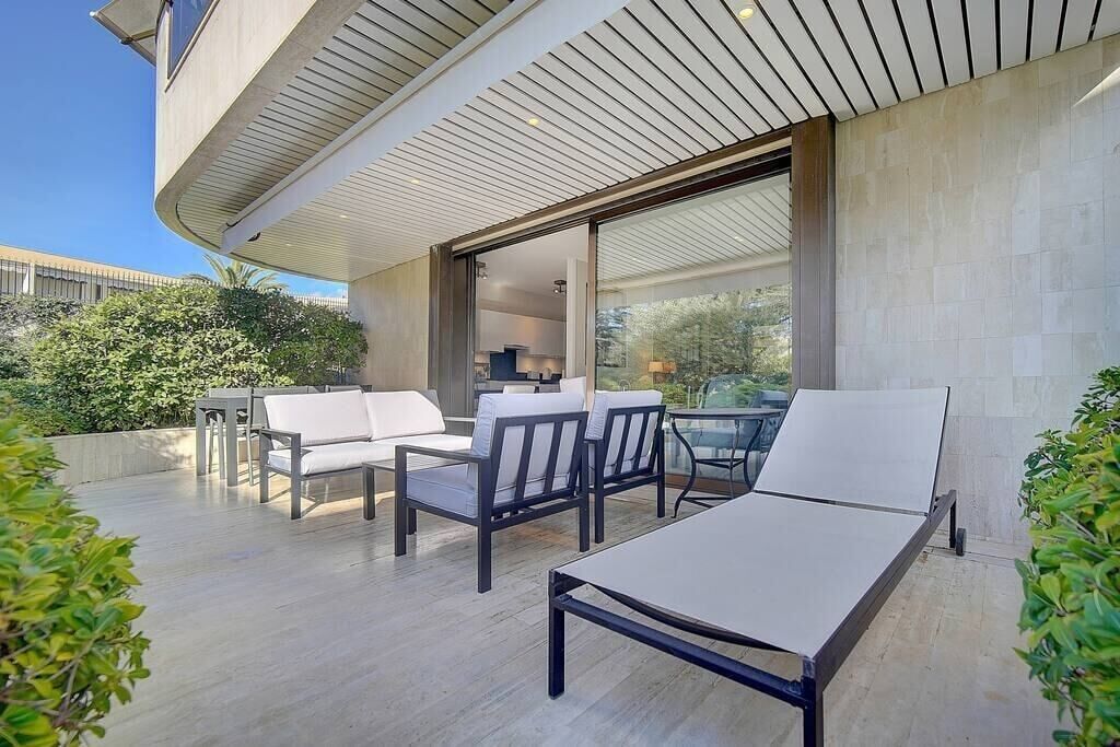 Un patio moderno al aire libre con zona de comedor, sillones de descanso y puerta de cristal que da a un espacio interior.