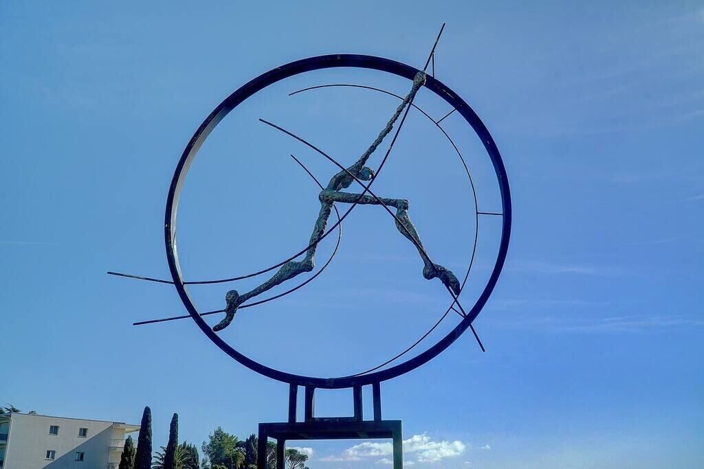 En stor, cirkelformad skulptur med en central figur, placerad mot en klarblå himmel.