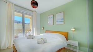 Une chambre d’hôtel avec un lit, une table de chevet, deux lampes fixées au mur et une vue sur l’extérieur, visible à travers une porte vitrée.