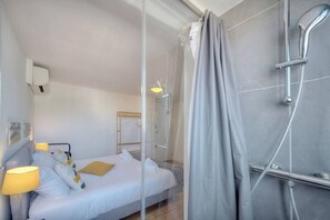 A modern hotel room with a bed, bedside lamp, and a shower area.