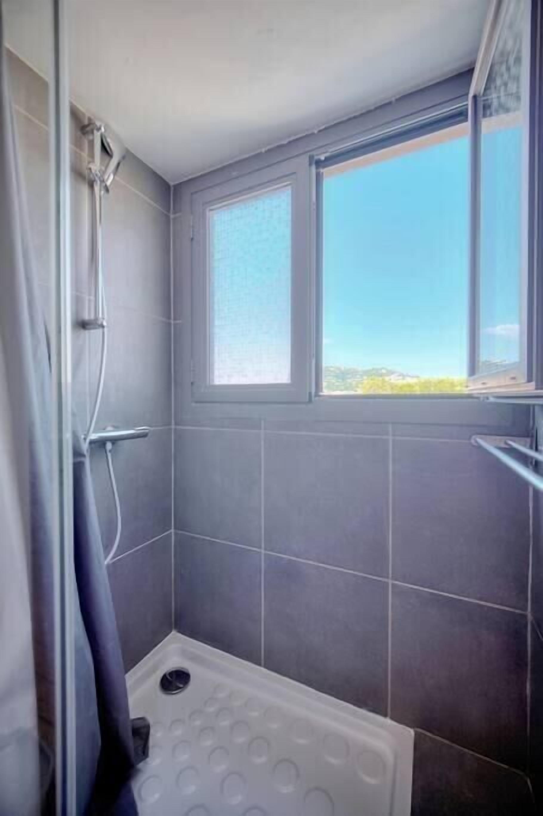 Une douche avec une fenêtre, des carreaux gris et une baignoire.