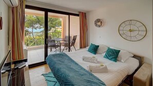 A hotel room with a bed, a desk with a keyboard, a chair, and a view of the outside balcony.
