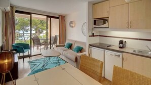A compact hotel room with a kitchenette, a sofa with cushions, a dining table, and a view of the outdoors.