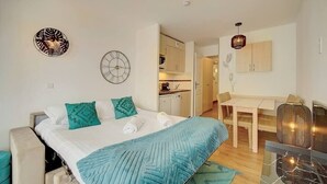 A modern bedroom with a bed, a desk, and a kitchenette.