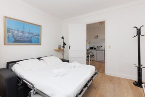 A neatly made bed with white linens, a black headboard, and a painting of a harbor scene on the wall. - Upstays Suquet AC 45m² Apartment (Cannes)