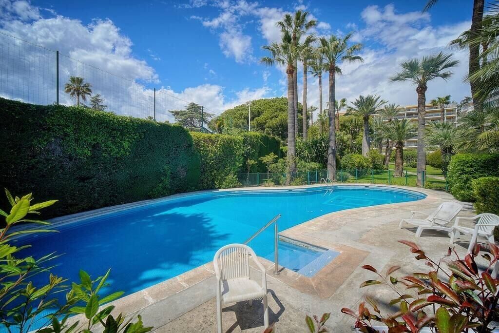 A swimming pool with a clear blue water, surrounded by palm trees and greenery.