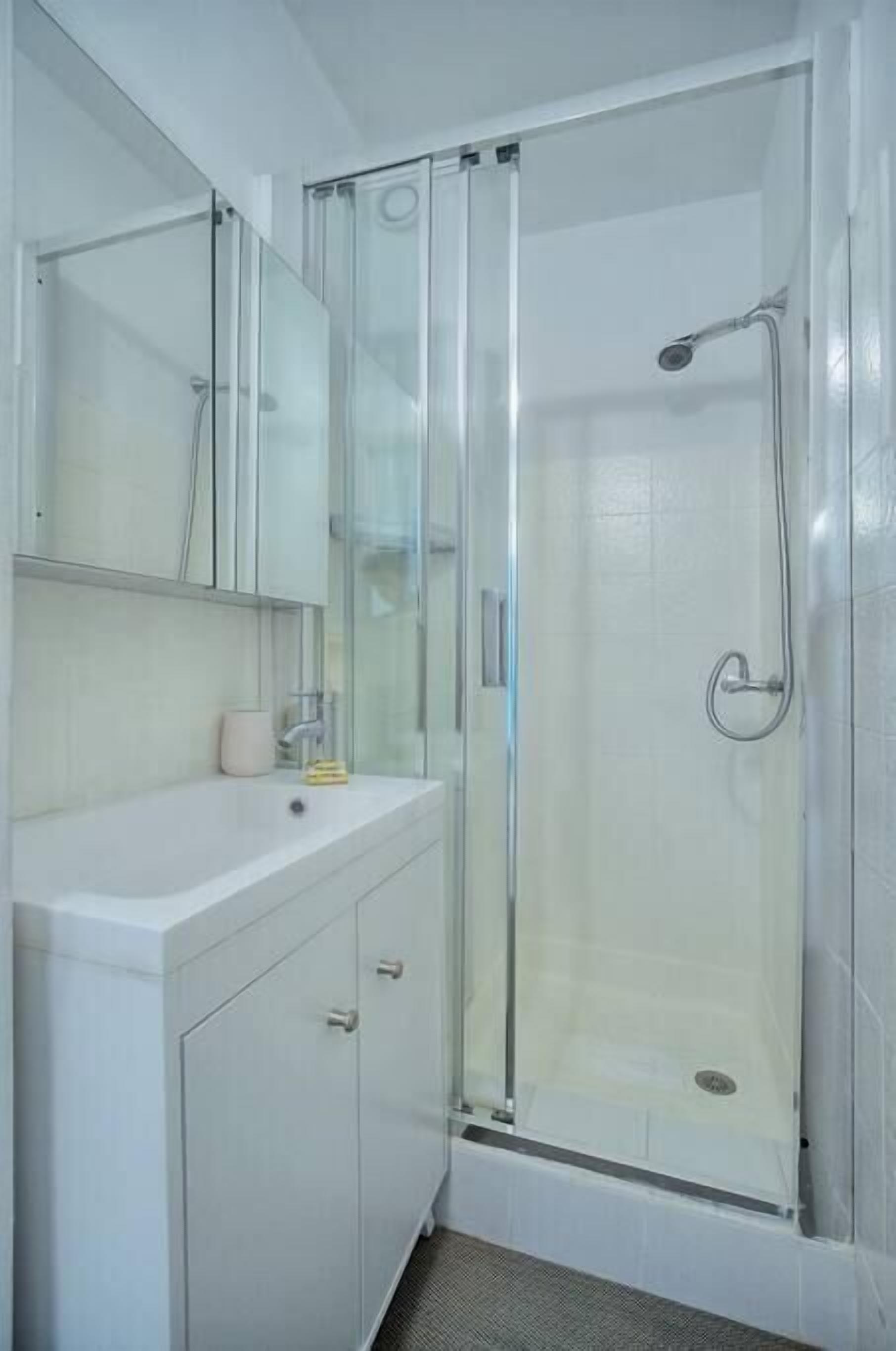 A modern bathroom with a glass shower enclosure, a white sink, and a mirror above the vanity.