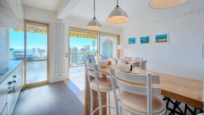 A modern kitchen with white cabinets, a wooden dining table, and pendant lighting. - Upstays Sea View Pool Terrace 75m² Apartment (Cannes)