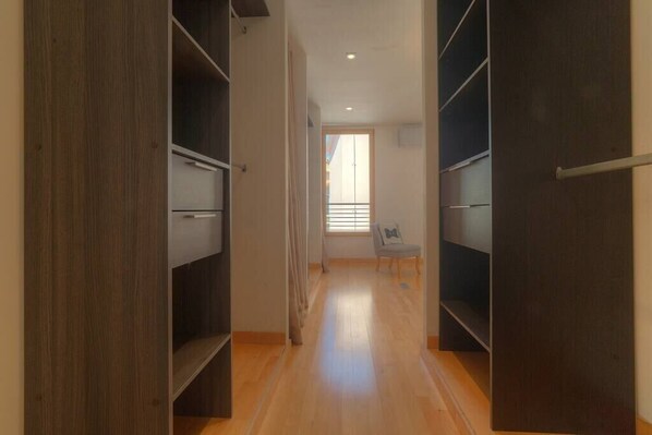 A hallway with wooden flooring, a chair, and open closet doors.