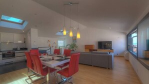 Eine moderne Küche mit Essbereich, einem grauen Sofa und einem Fernseher im Wohnbereich.