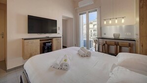 A hotel room with a bed, a flat-screen TV mounted on the wall, a small kitchenette, and a balcony with a view of buildings. - Upstays Terrace 24m² Studio Carnot (Cannes)