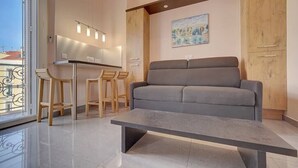 A modern living room with a grey sofa, a coffee table, and wooden chairs. - Upstays Terrace 24m² Studio Carnot (Cannes)