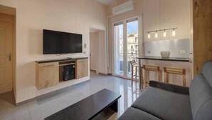 A modern living room with a flat-screen TV, a sofa, a coffee table, and a kitchen area with a dining table and chairs. - Upstays Terrace 24m² Studio Carnot (Cannes)