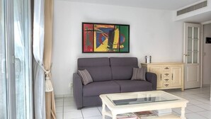 Un salon avec un canapé gris, une table basse en verre et un tableau abstrait aux couleurs vives accroché au mur.
