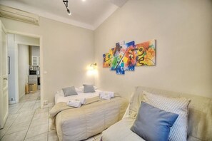 Une chambre d’hôtel avec un lit, un canapé, une œuvre d’art accrochée au mur et, au fond, une petite cuisine.