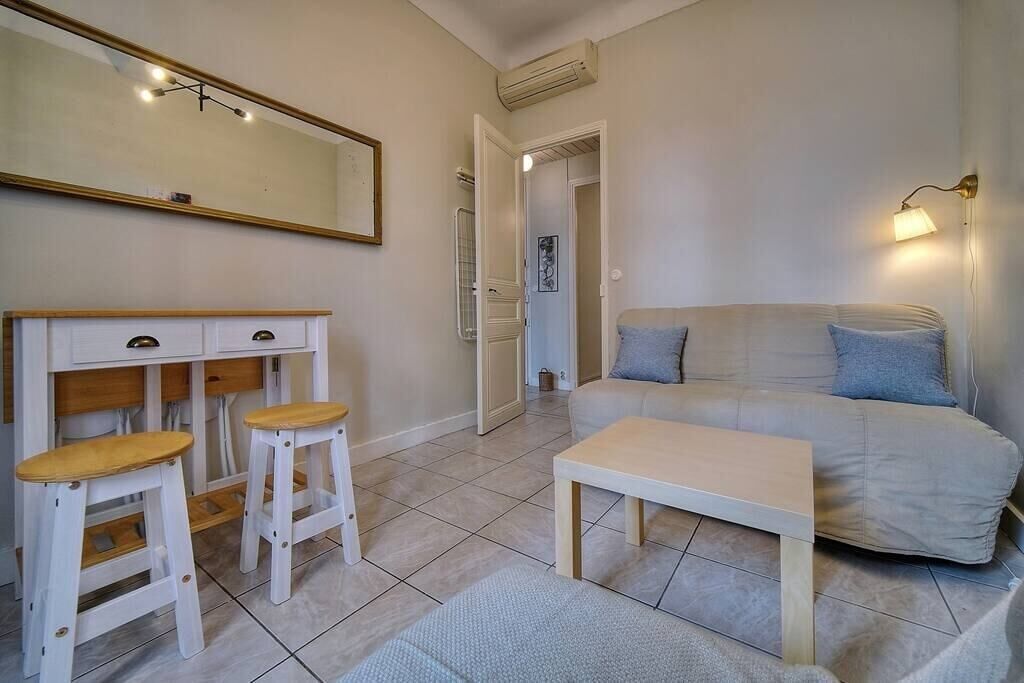 Un salon comprenant un canapé, deux tabourets en bois, une petite table, un miroir et une lampe fixée au mur.