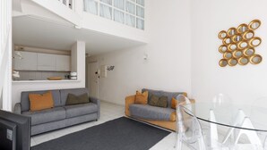 Un espacio moderno para vivir con un sofá gris, un sofá más pequeño, una mesa de comedor de vidrio y una zona de cocina.