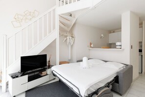 A modern bedroom with a bed, a TV, a desk, and a staircase.