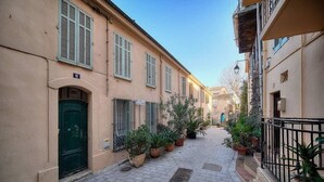 A narrow street with buildings on either side, potted plants lining the path, and a green door on the left. - Upstays cosy 20m² Apartment Suquet (Cannes)