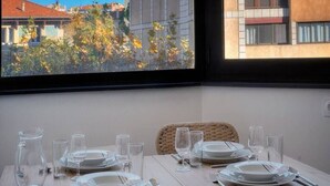 A dining table set with plates, glasses, and cutlery, positioned near a window overlooking a cityscape. - Immogroom - Charming apartment - Close to beaches (Cannes)