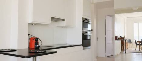 A modern kitchen with white cabinetry, a black countertop, and stainless steel appliances including an oven and a coffee machine.
