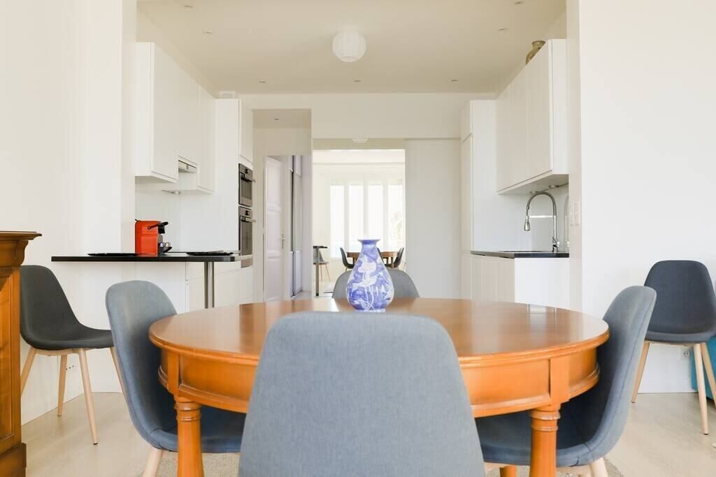 A modern dining area with a wooden table, grey upholstered chairs, and a blue vase centerpiece.