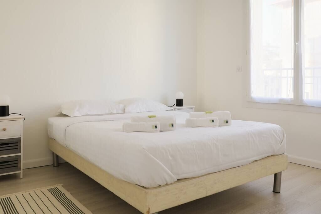 A clean, white bedroom with a bed, bedside tables, and a window.