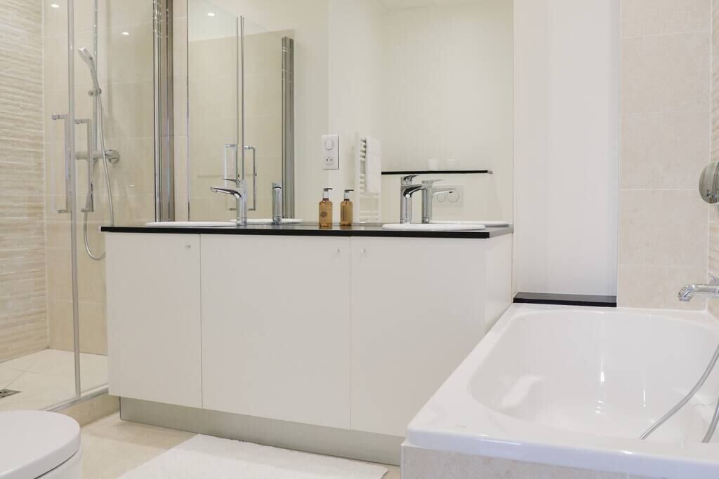 Une salle de bain moderne avec une douche à parois de verre, une baignoire blanche et un meuble-lavabo doté d’un plan de travail noir.