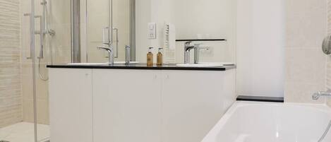 Une salle de bain moderne avec une douche à parois de verre, une baignoire blanche et un meuble-lavabo doté d’un plan de travail noir.