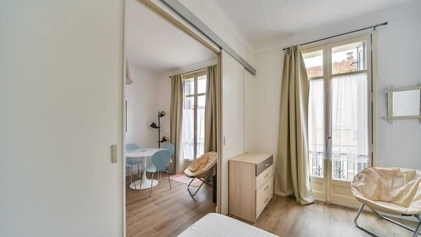 A modern hotel room with a bed, a desk, a chair, and a balcony with curtains.