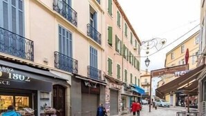 A narrow street with buildings on either side, some shops, and a few people walking.