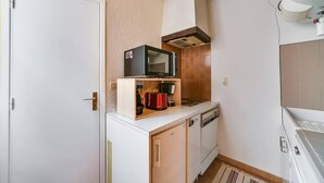 A compact kitchen with white cabinetry, a microwave on a shelf, and a red appliance on the counter.