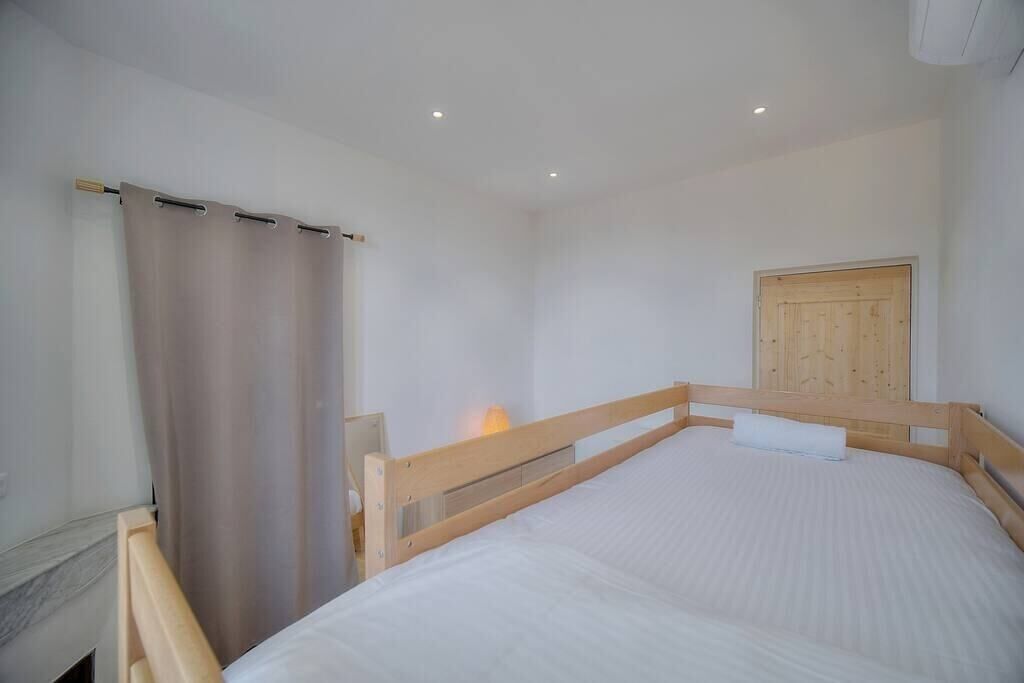 A bedroom with a wooden bed, a curtain, a wall-mounted light, and a wooden door.