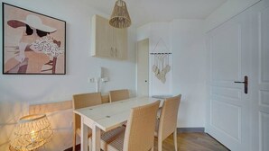A dining area with a white table and wicker chairs, a hanging light fixture, and a wall-mounted cabinet. - Upstays Terrace Pool 37m² Apartment (Cannes)
