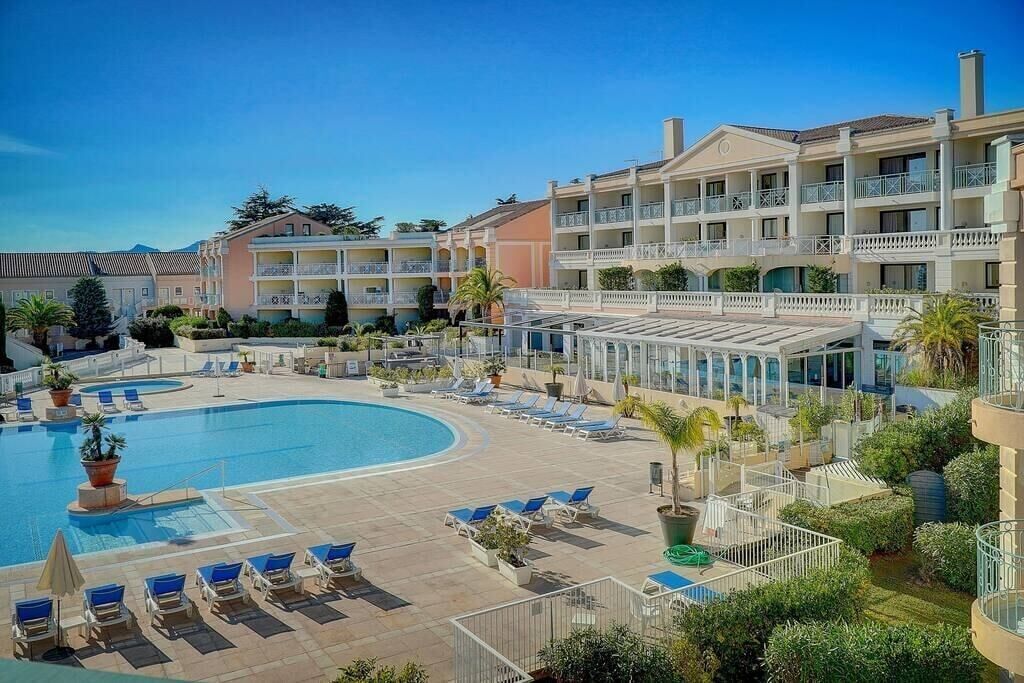 Ein Hotel mit großem Schwimmbad, Liegestühlen und einem gepflegten Garten.